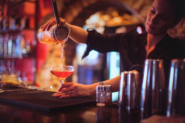 Close-up of a young female bartender pouring cocktail in a nightlife cocktail bar.