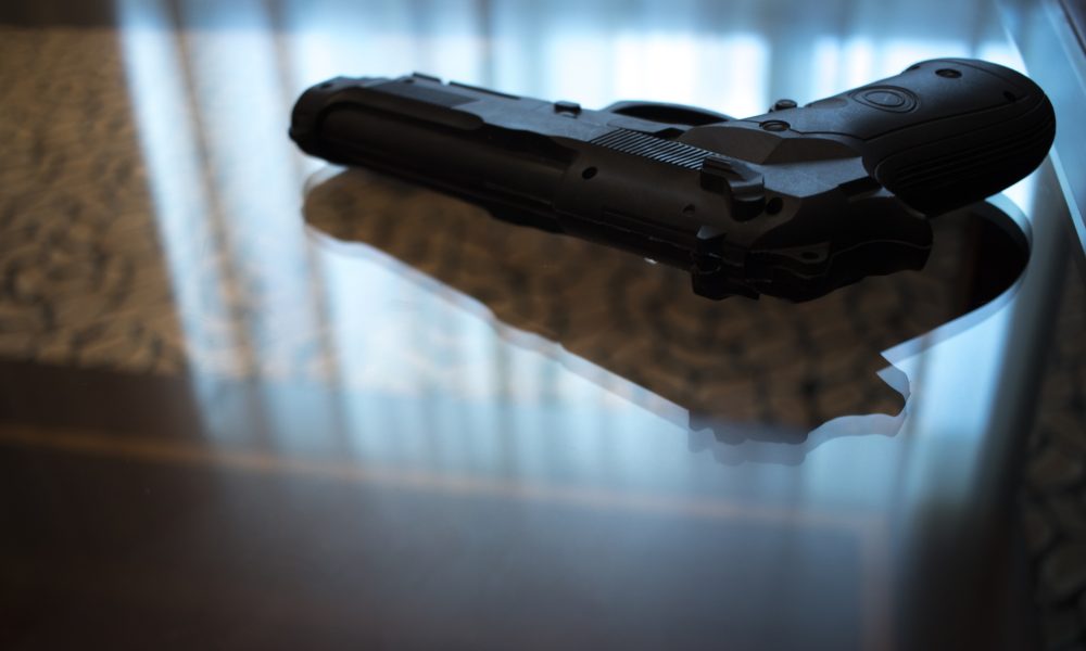 Automatic pistol gun on glass table in bedroom in luxury hotel in silhouette with reflection of window light.
