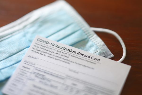 A blank COVID-19 vaccination record card rests on top of a protective face mask.