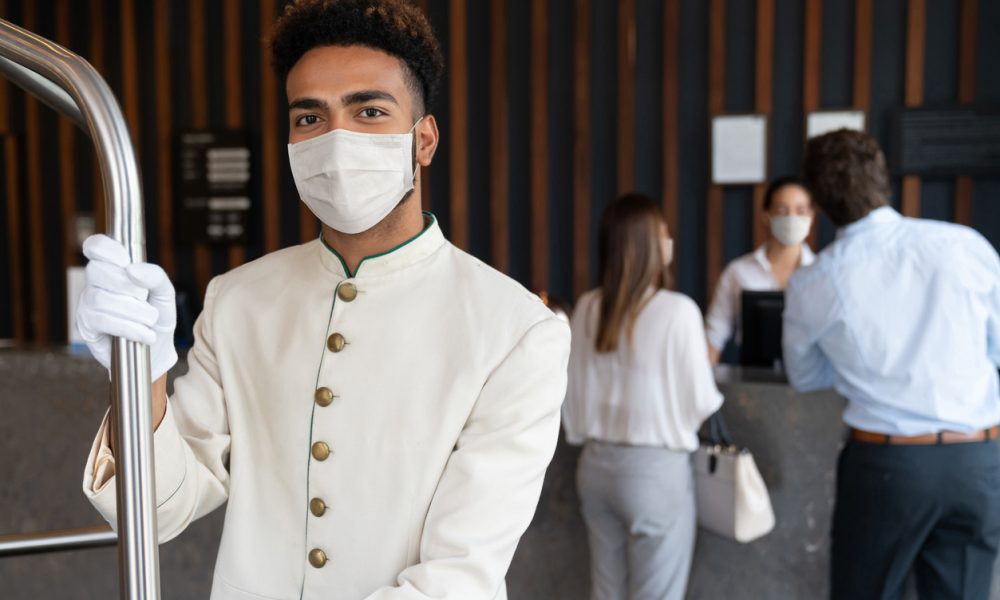 Portrait of a happy bellboy working at a hotel and wearing a facemask to avoid COVID-19 - service concepts