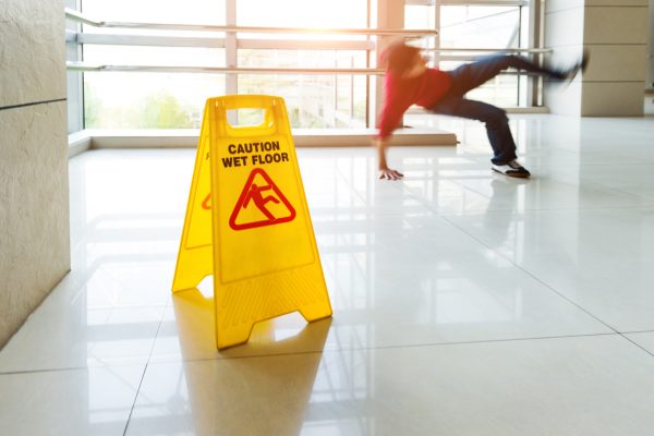 Man slips falling on wet floor next to the wet floor caution sign.