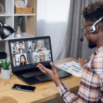 Multiethnic group of people having business meeting through video call on laptop. View from shoulder of black man sitting at home office and working remotely.