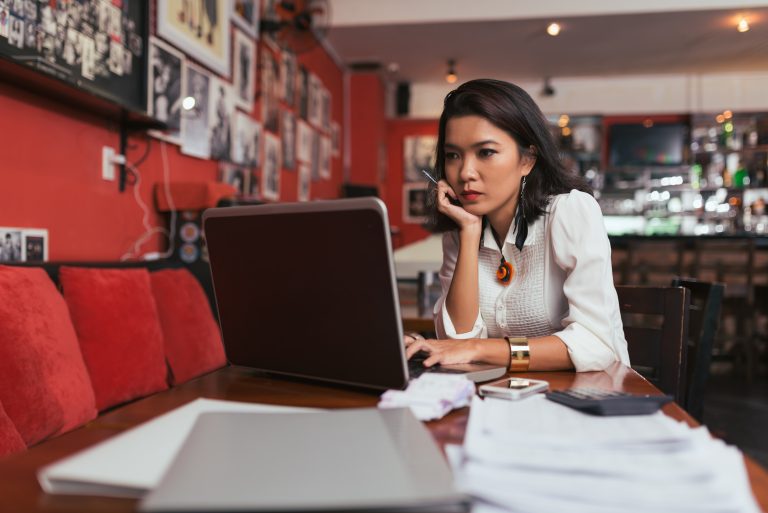 Pensive Asian bar owner using laptop to pay bills online