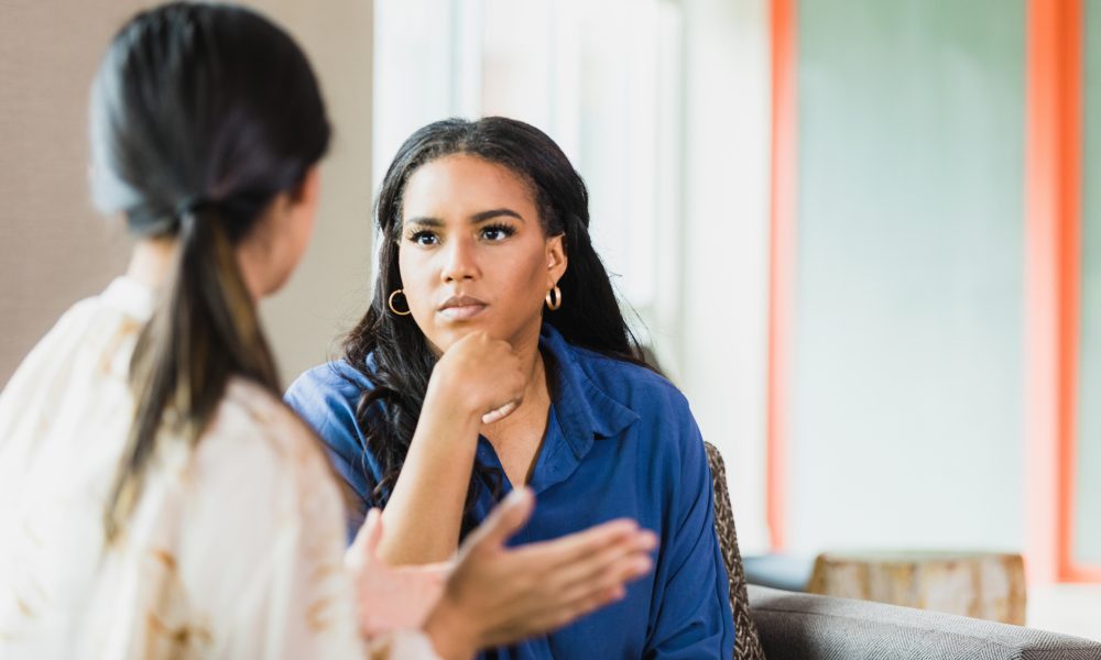 During a counseling session, the unrecognizable mid adult female patient gestures while speaking. The mid adult female therapist listens attentively.
