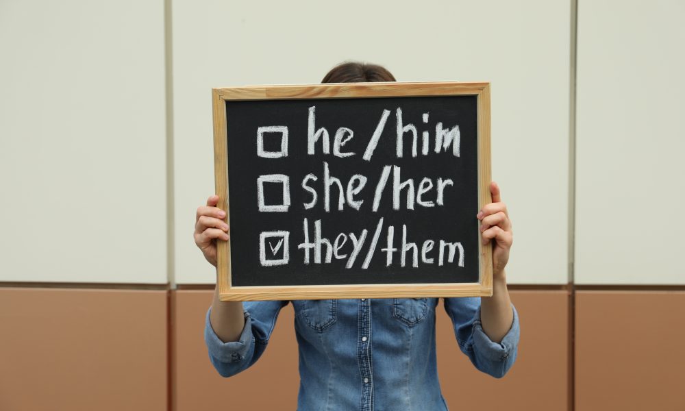 Woman holding chalkboard with list of gender pronouns near color wall