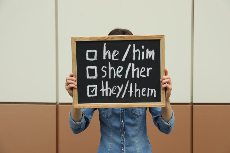 Woman holding chalkboard with list of gender pronouns near color wall