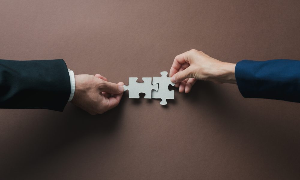 Teamwork and partnership conceptual image - hands of a businessman and businesswoman joining blank matching puzzle pieces over brown background.