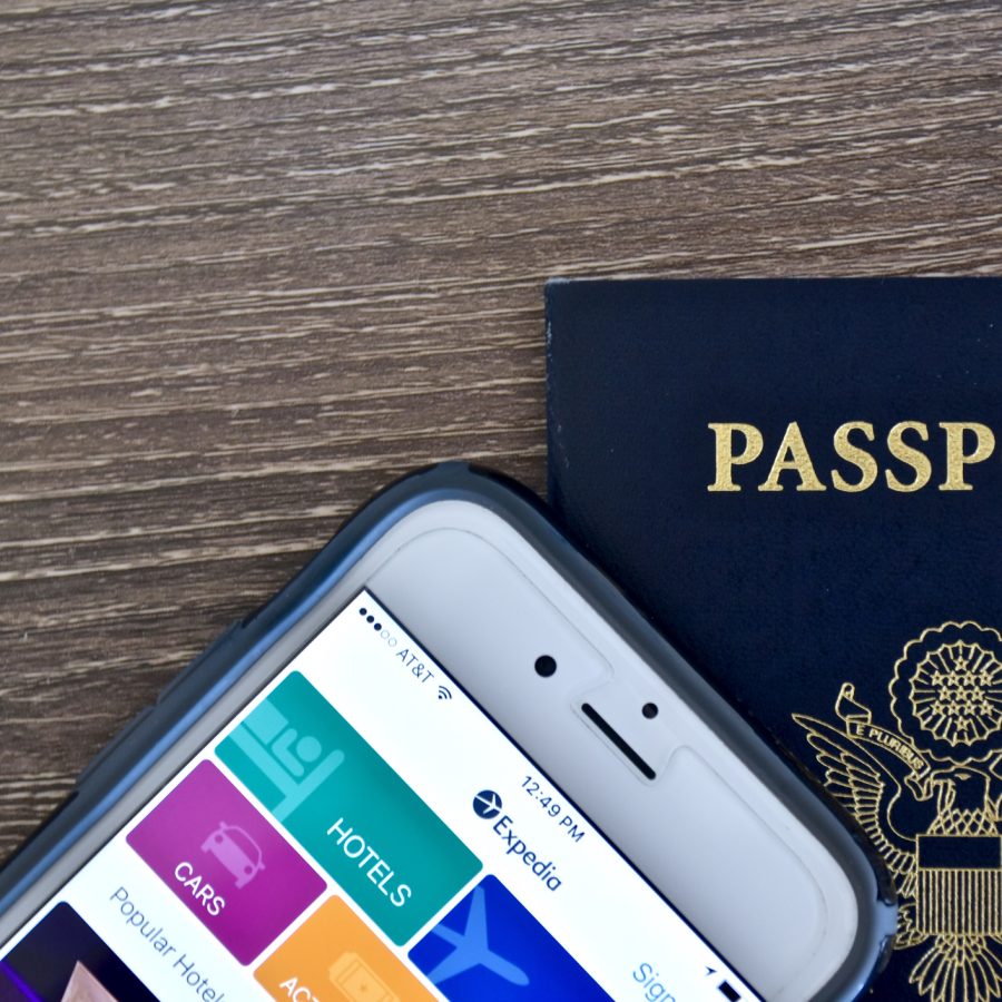 An Apple iPhone 6s displaying the Expedia application homepage on the screen while laying next to an American passport.