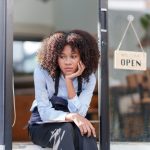 Female shopkeeper sitting stressed out at the store entrance frustrated