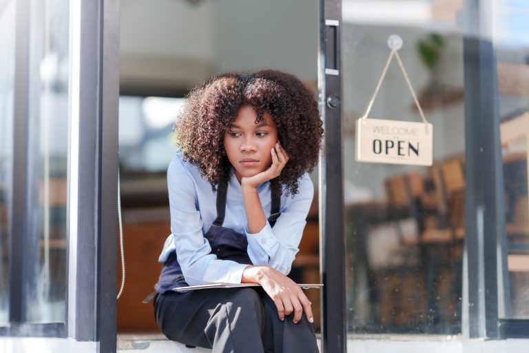Female shopkeeper sitting stressed out at the store entrance frustrated