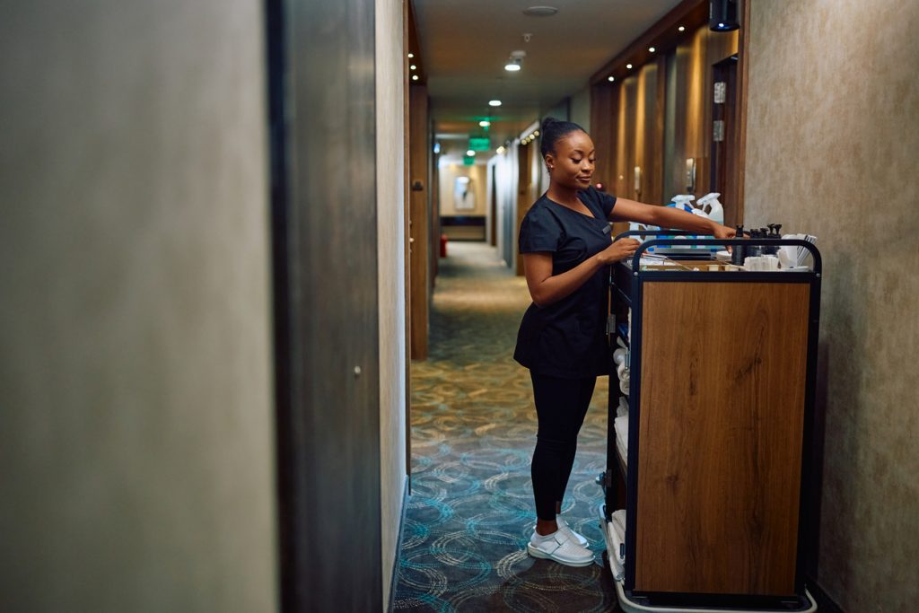 Black female housekeeper replenishing toiletries in guest rooms in a hotel