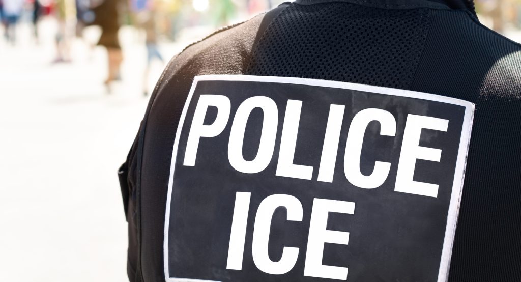 Ice Police Immigration and Customs Enforcement - Close-up of POLICE ICE marking on the back of a hi-visibility stab proof vest worn by a police officer at the scene of an incident - HospitalityLawyer.com®