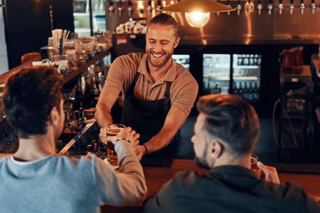 Top view of bartender serving beer to young men - HospitalityLawyer.com®