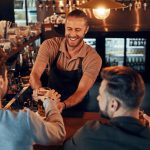 Top view of bartender serving beer to young men - HospitalityLawyer.com®