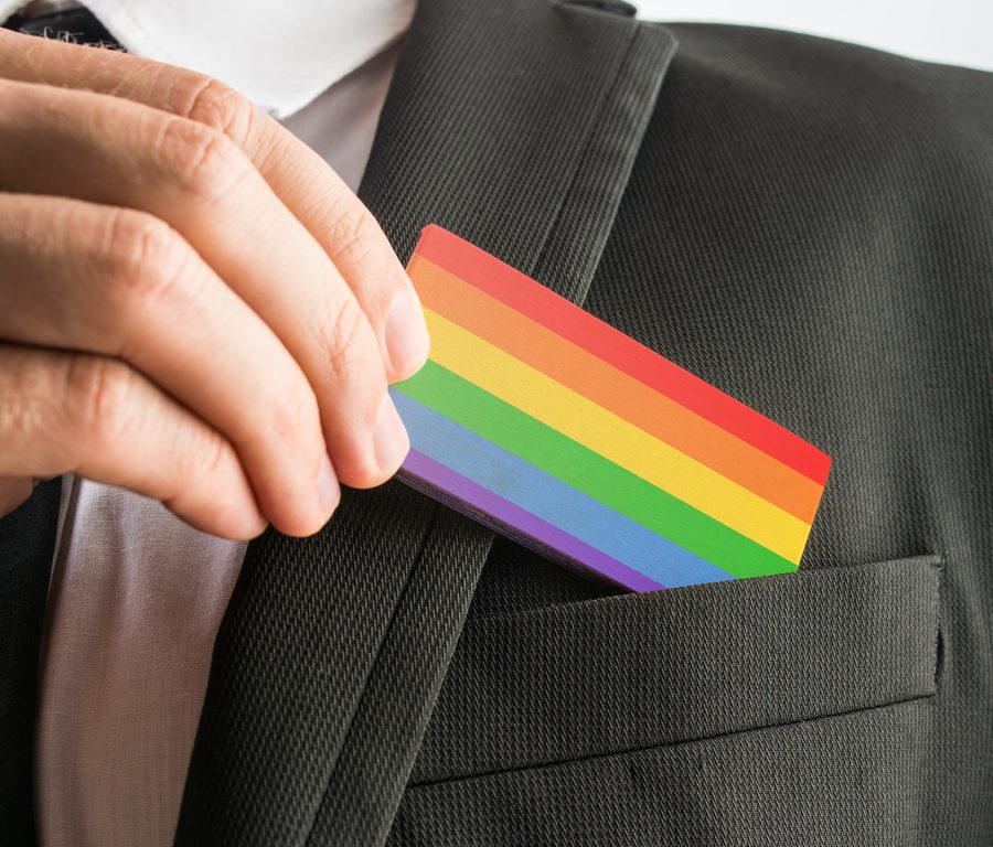 Person in a suit slides a rainbow pride card into the breast pocket, signaling LGBTQ+ pride in a professional setting.